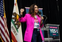 A woman in a bright pink blazer with a raised fist standing in front of a California and USA flag