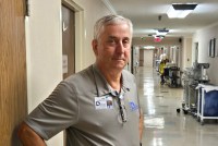 A photo of an older man standing for a portrait in a hospital corridor.