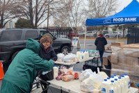 A photo of food bank attendees picking up loaves of bread, half-gallons of milk, and bags of produce.