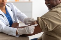 A photo of an older man having a bandage placed on his arm after receiving a vaccine.