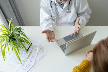 A doctor conversing with a patient. The doctor has a laptop in front of him.