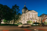 A photo of Indiana's Capitol taken at night as a car drives on the road in the foreground.