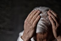 A photo of an older man leaning forward, his hands on his head.