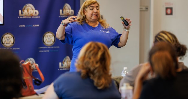 A woman wearing a blue shirt stands in front of a group of people as she gives a presentation
