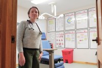 A physician stands in an examination room at a clinic. She has a stethoscope draped over her neck.
