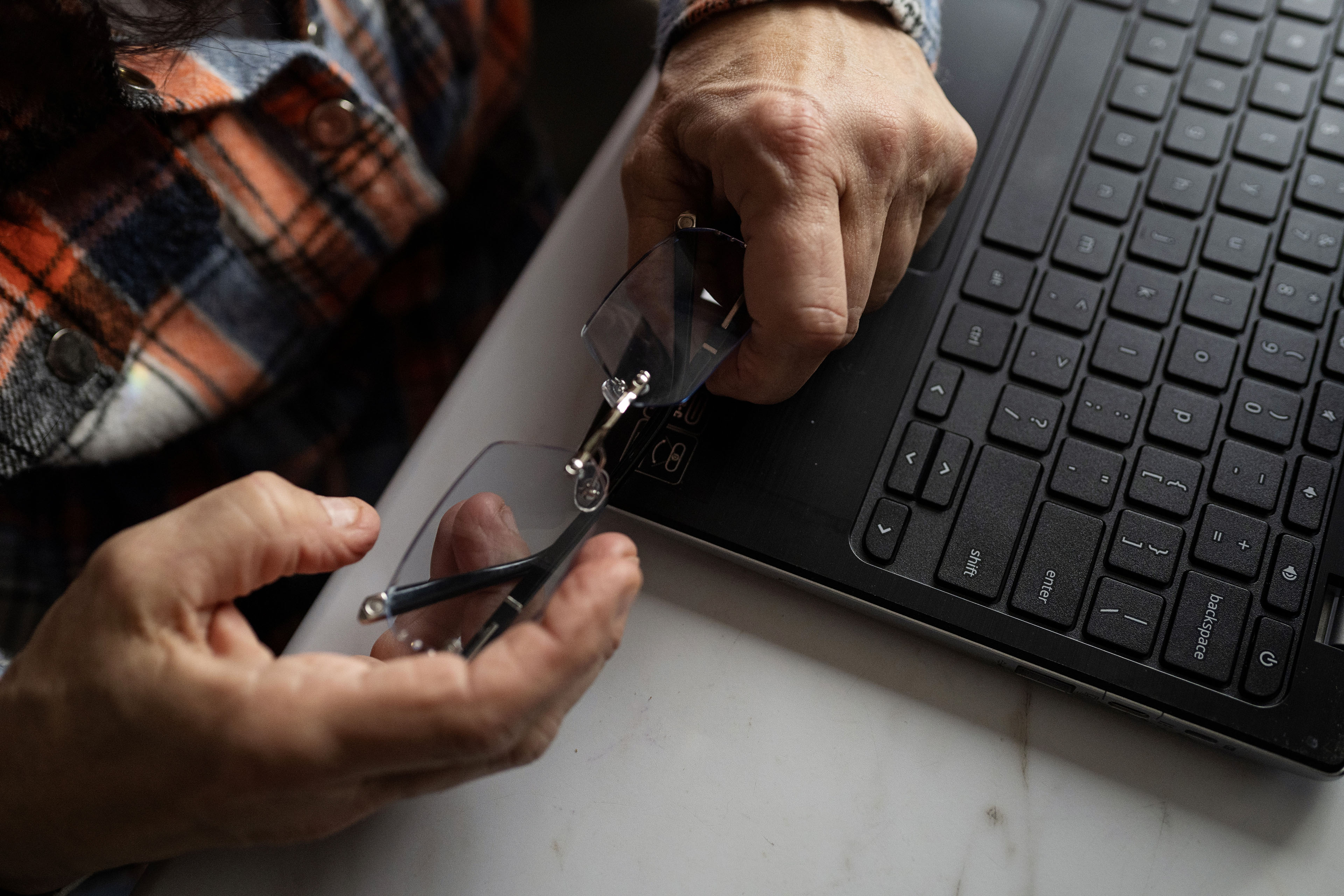 A woman holds eye glasses in her hands, beside her laptop.