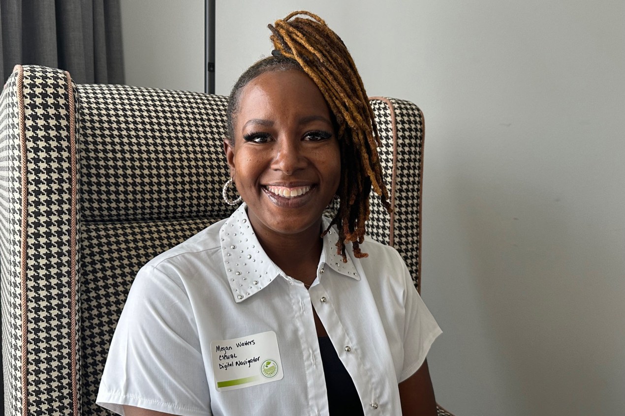 A portrait of a woman smiling at the camera and wearing a white blouse with a name tag.