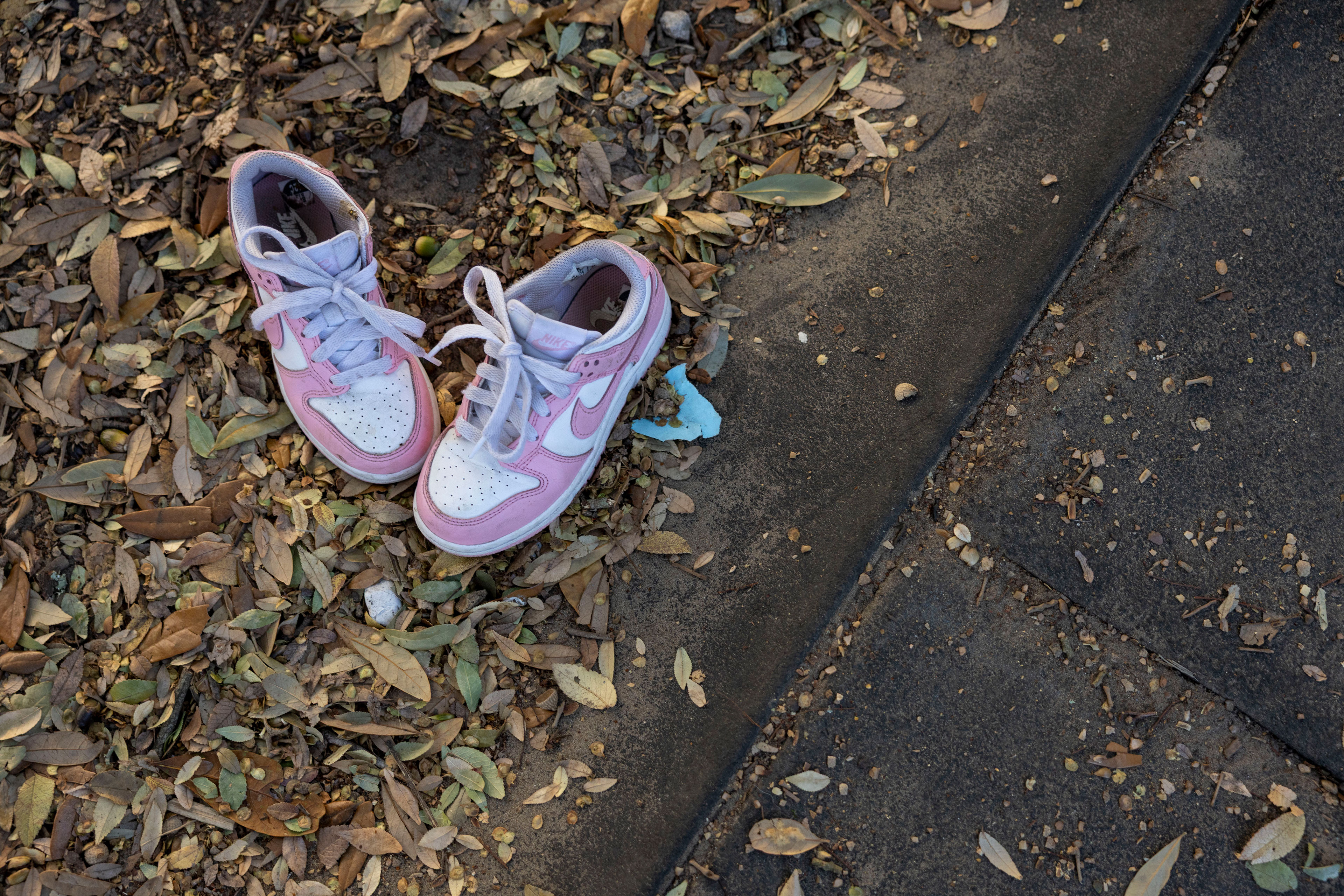 A pair of pink and white sneakers are placed on the ground beside playground tiles.