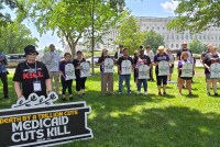 A group of protesters stand holding signs. One large sign reads, "Death by a trillion cuts: Medicaid cuts kill." Others hold signs shaped like tombstones that read, "Here lies America's future," and "R.I.P. Sacrificed for the rich."