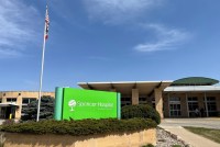 A photo of a hospital exterior with a neon green sign in front of it that reads, "Spencer Hospital, healthier together."