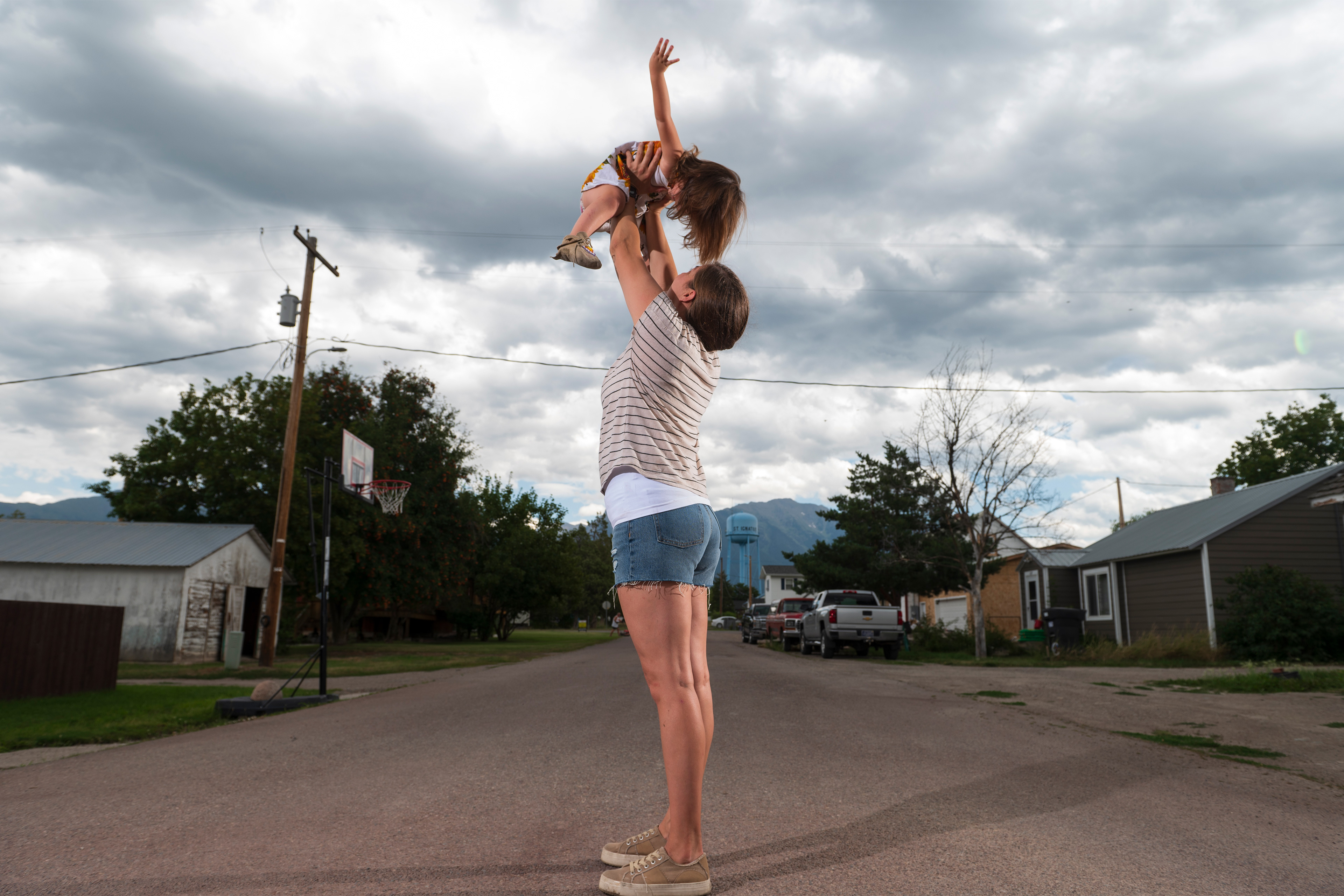 A photo of Jonnell Wieder holding up her daughter to the sky as they play on their street.