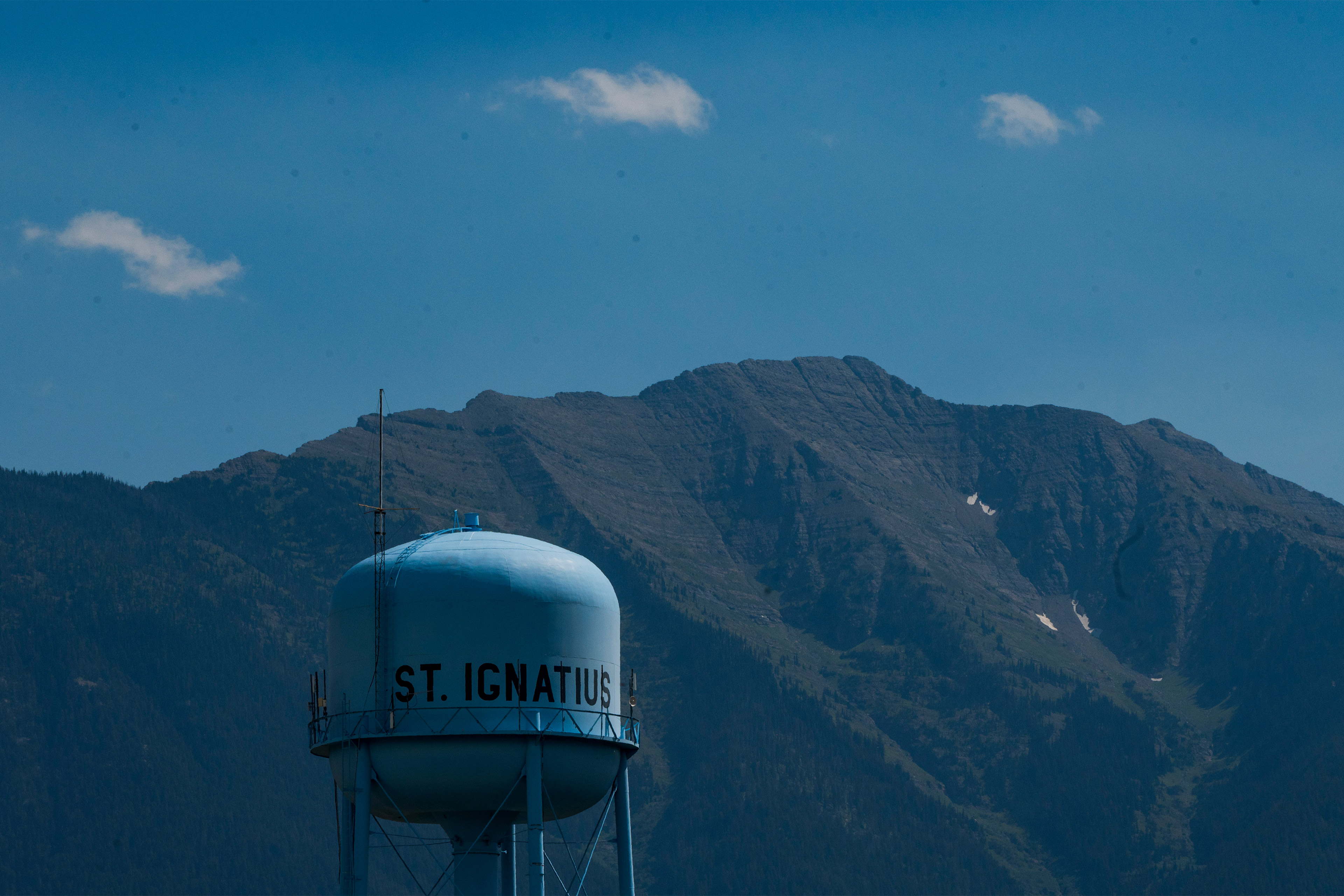A photo of a water tower in rural Montana. Mountains are seen behind it.