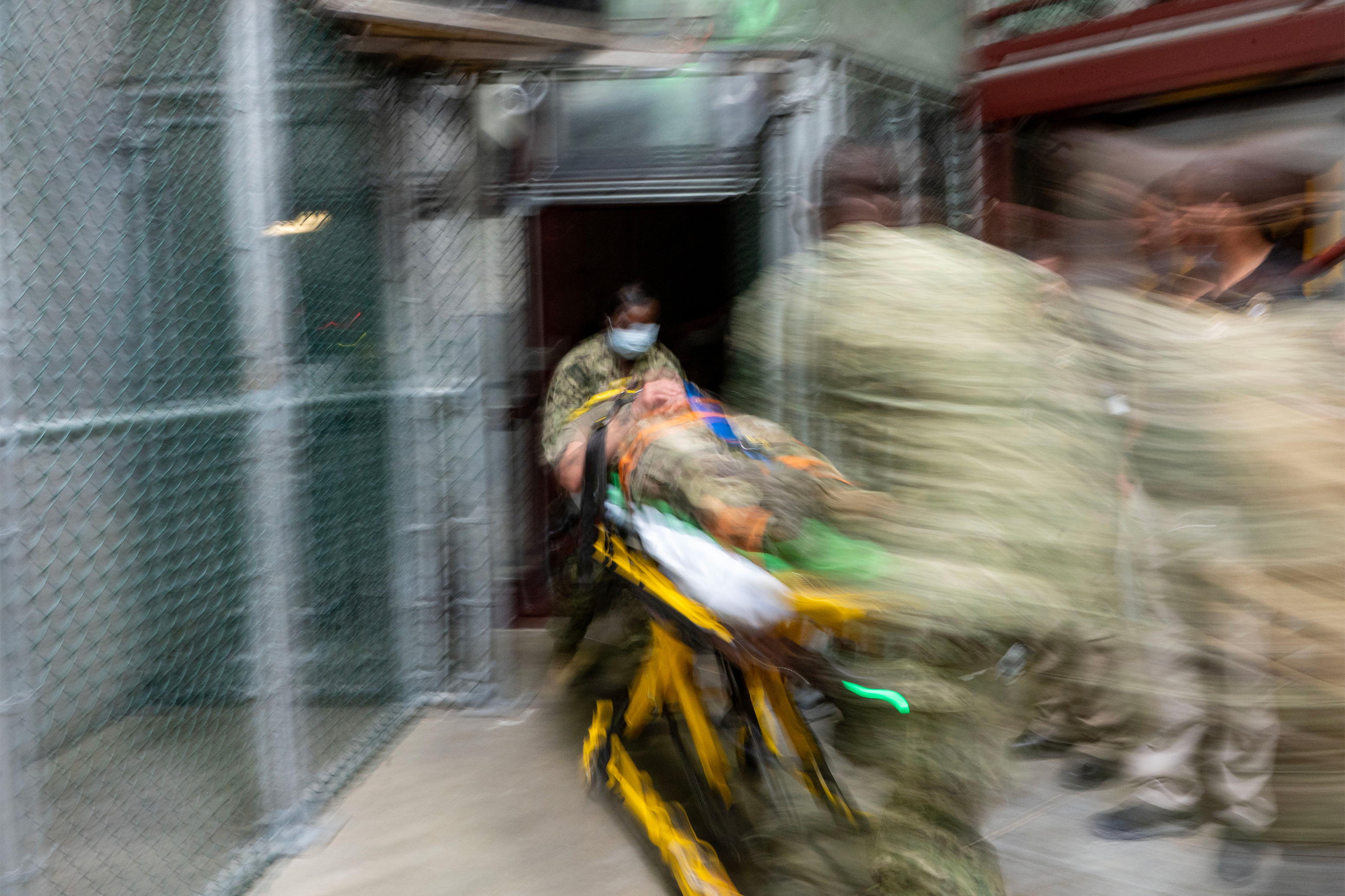 A photo with motion blur showing a gurney being pushed by medics in camo uniforms.
